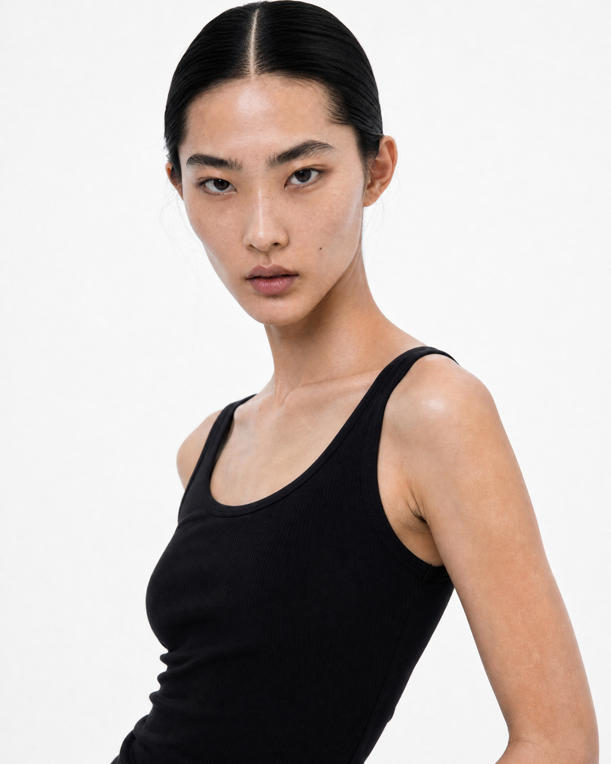 Portrait of a woman with slicked-back hair in a black sleeveless top, facing slightly to the left against a white background.